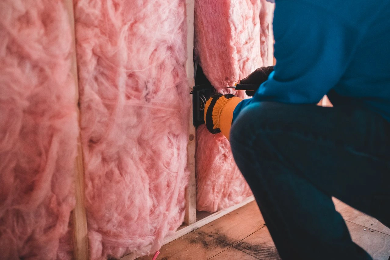 Worker fitting fiberglass batt insulation between wooden wall studs in charleston.